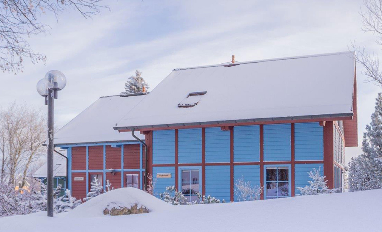 Außenansicht von drei modernen Ferienhäusern des Sporthotels Oberhof im Winter eingebettet in der verschneiten Landschaft des Thüringer Waldes
