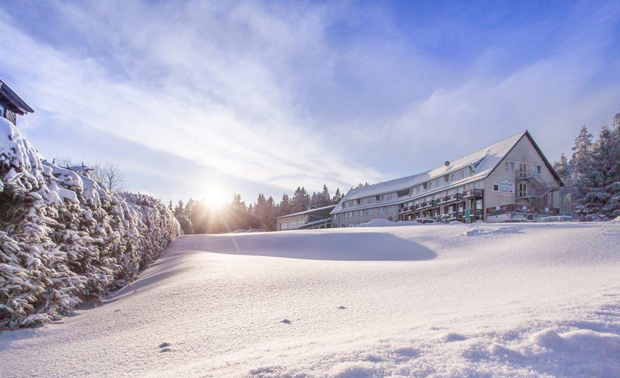 Außenansicht vom kompletten Sporthotel Oberhof eingebettet in der verschneiten Winterlandschaft des Thüringer Waldes