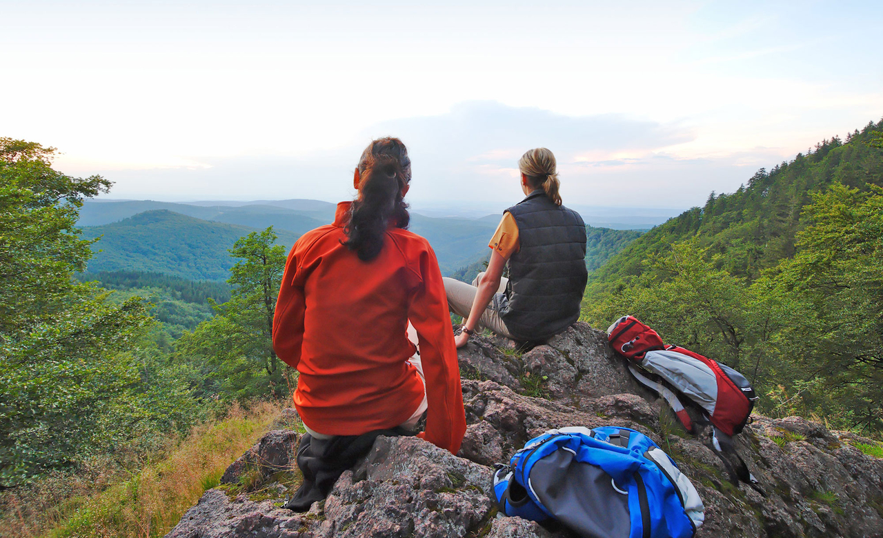 zwei Wanderer sitzen auf einem Felsen auf einem Berg im Thüringer Wald und blicken auf die umliegende Landschaft und Berge