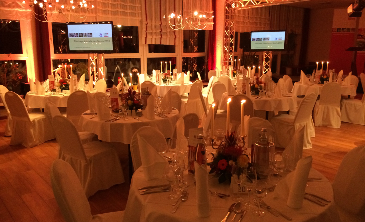 Veranstaltungsraum im Sporthotel Oberhof mit weiß eingekleideten Tischen und Stühlen mit festlicher Dekoration für eine Abendveranstaltung